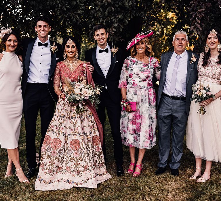 Bride & groom stand with guests outdoors in colourful outfits after wedding ceremony