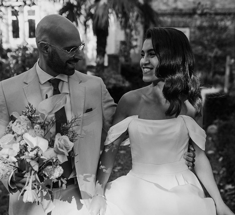 Bride in a structured wedding dress with off the shoulder detail walking with the groom 