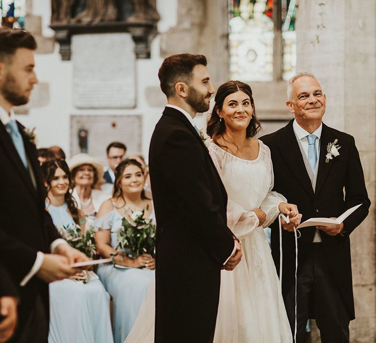 Bride, father of the bride, groom and best man stand at the altar for the beginning of the church wedding ceremony