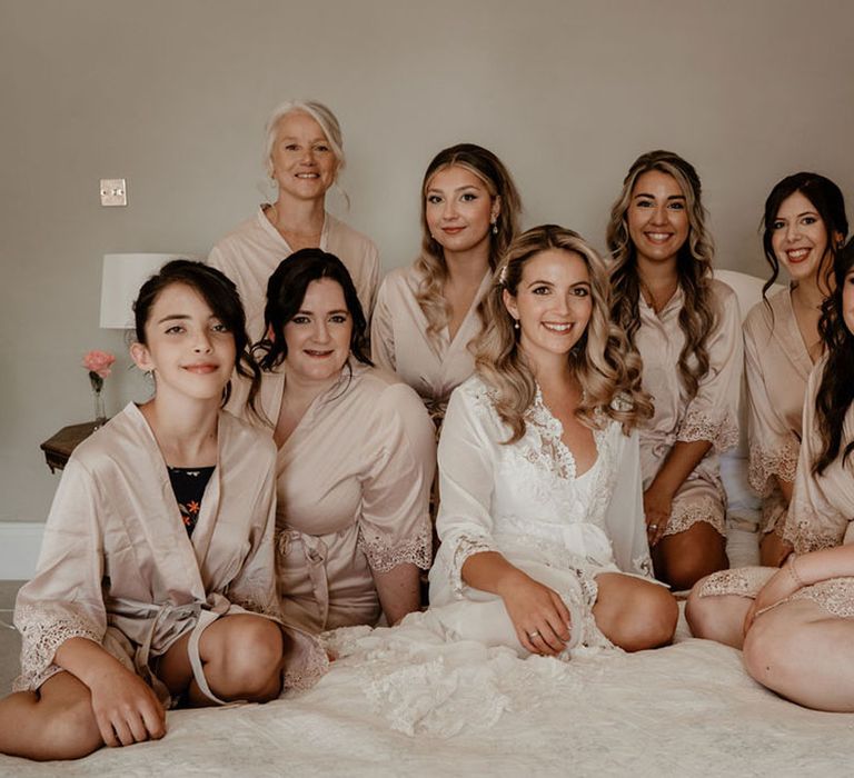 Bridesmaids in champagne gold robes with the bride in a white robe sit to get ready for the wedding 