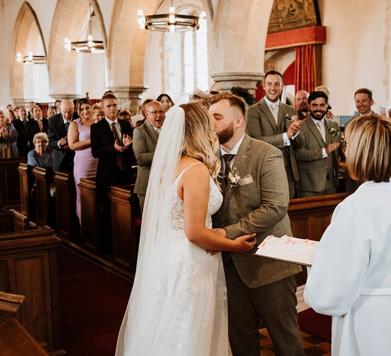 The wedding guests stand and applaud as the bride and groom share their first kiss as a married couple 