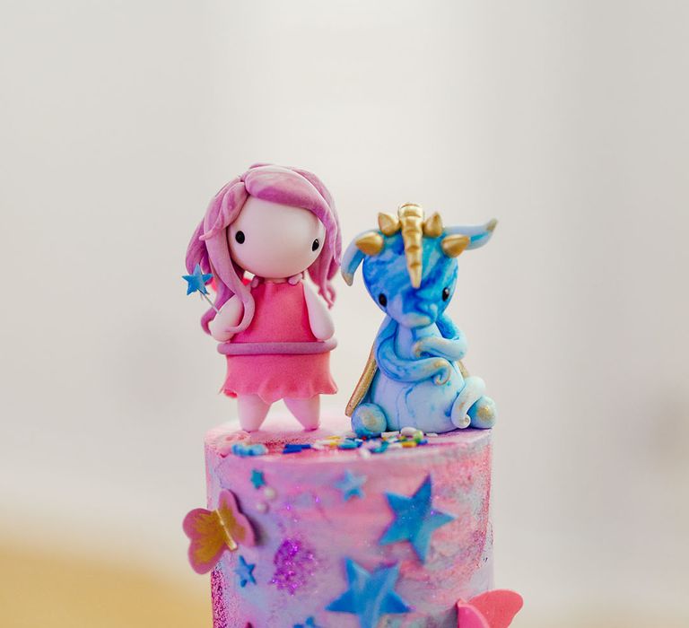 Personalised wedding cake toppers; one pink cartoon girl with pink dress and pink hair, and the other a small blue unicorn with a gold horn 