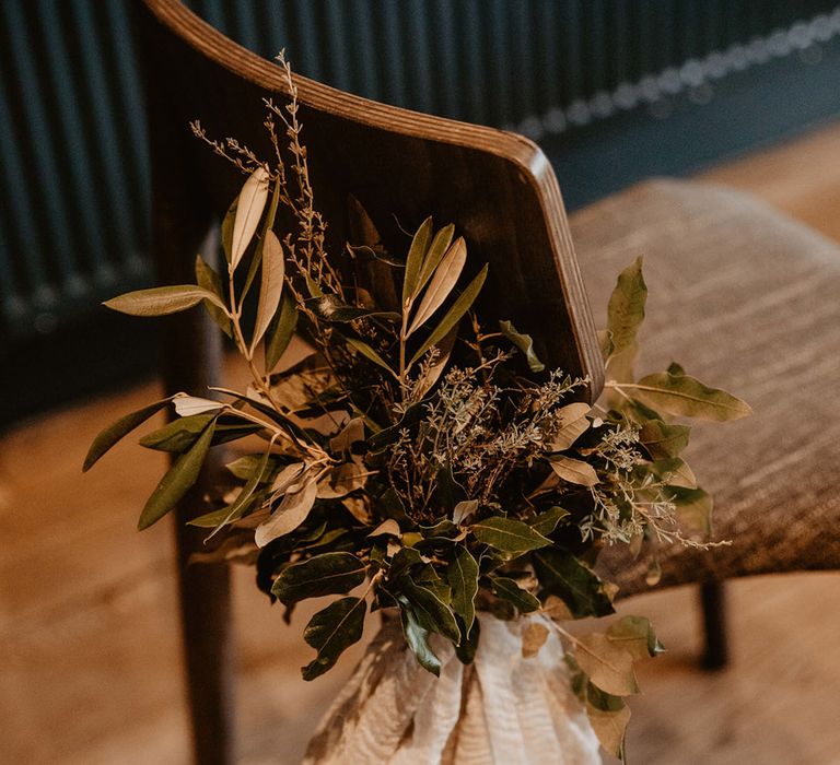 Wedding foliage decorating the wooden wedding chair with cream ribbon 