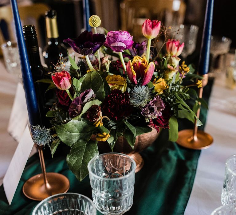 Emerald green table runner with dark blue taper candles with a spring wedding flower arrangement decorating the wedding tables 