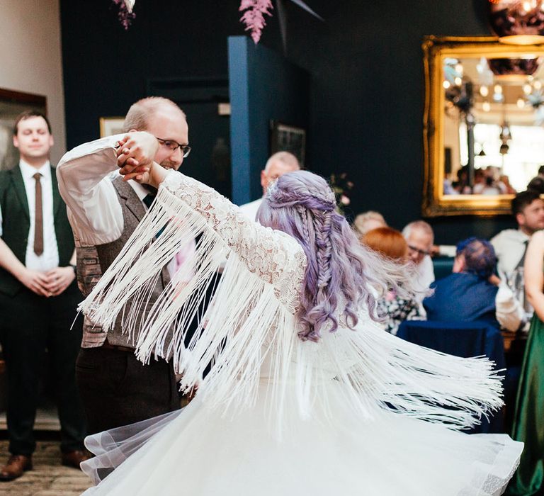 Groom twirling bride in midi-length bridal gown with lace embroidered sleeves and large white fringing along the sleeves and polka dot wedding boots