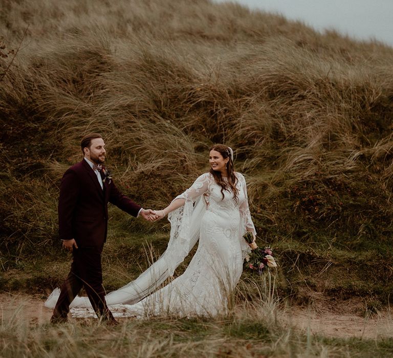 The bride and groom walk along the coast in Northumberland on their wedding day 