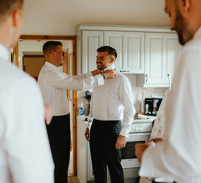 The groom and groomsmen all get ready together in the morning and help each other put on their ties 