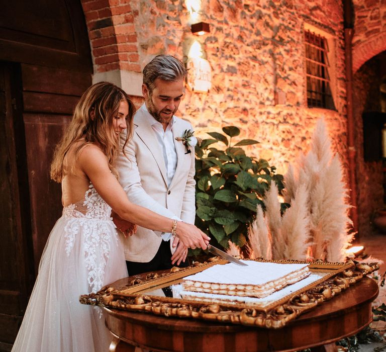 Bride in sparkly wedding dress with groom cutting the wedding cake at outdoor wedding reception