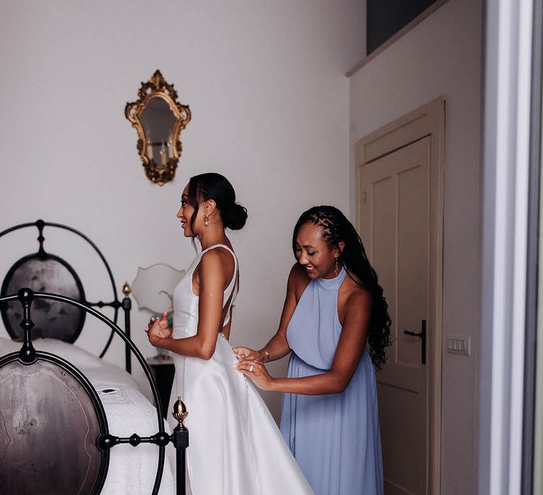 bridesmaid in blue dress helping the bride into her Jane Hill bridal gown