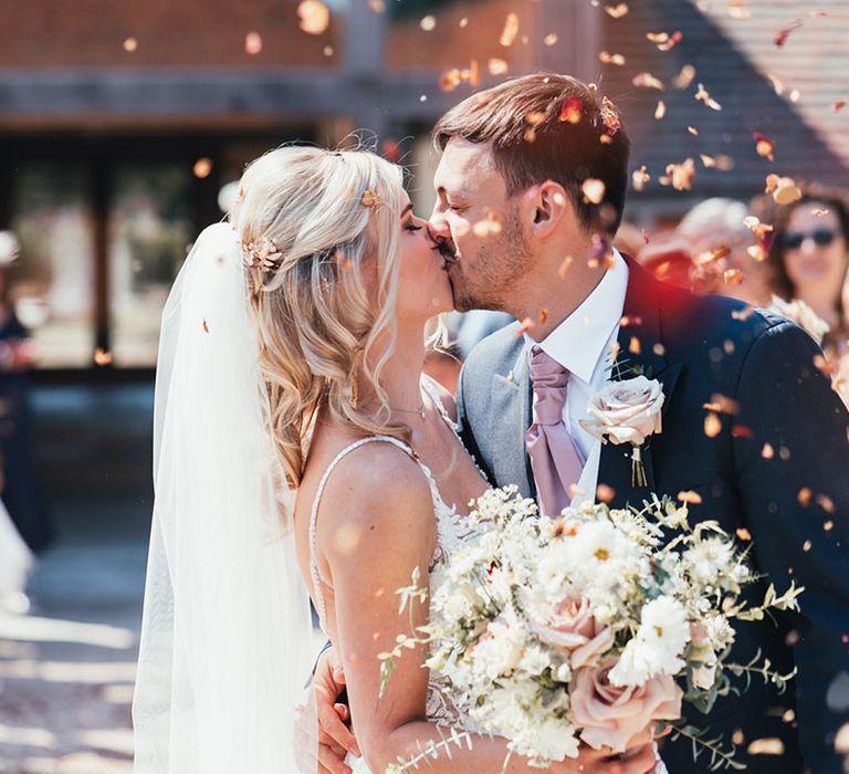 The bride and groom share a kiss together as confetti is thrown around them 