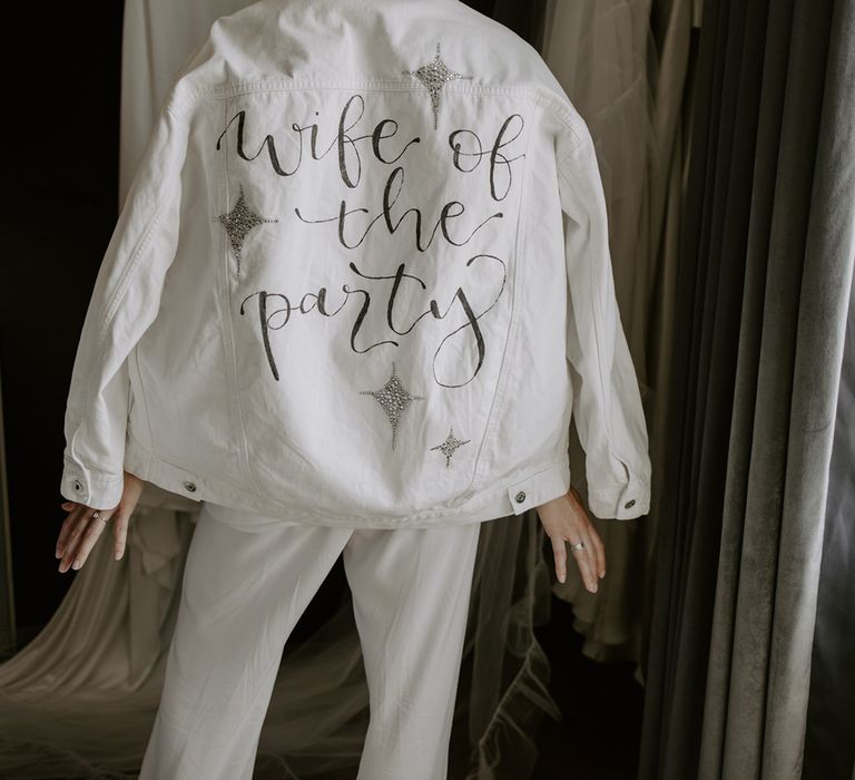 Bride wearing a customised white bridal denim jacket reading 'Wife of the Party' with sparkly details 