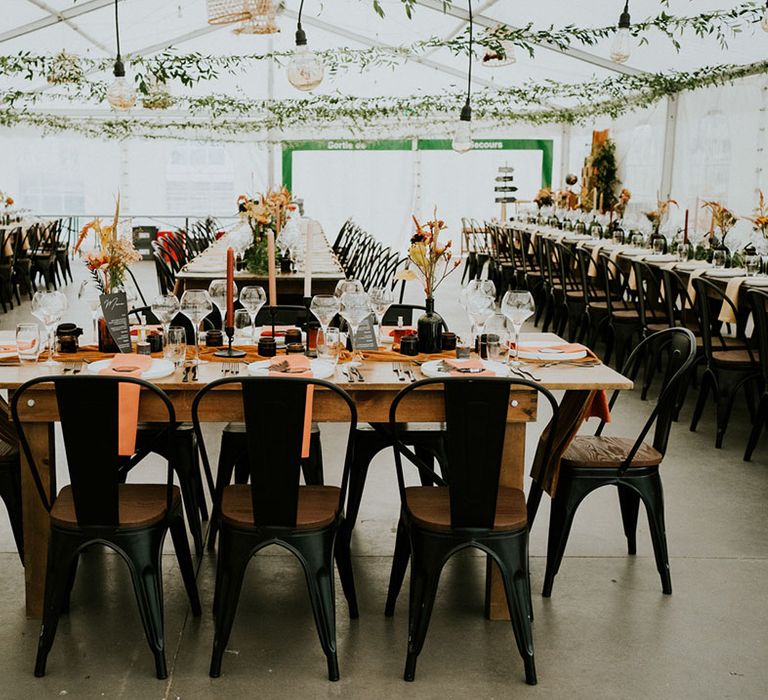 boho wedding reception decorations with industrial chairs, hanging foliage and orange and black wedding decor 