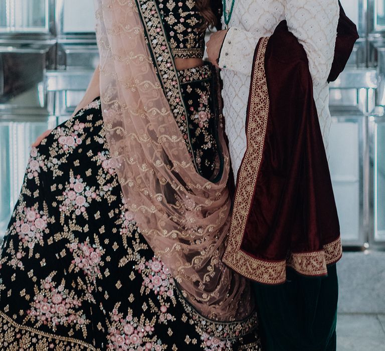 Bride in two piece black and gold patterned saree posing with groom in white and gold patterned sherwani  