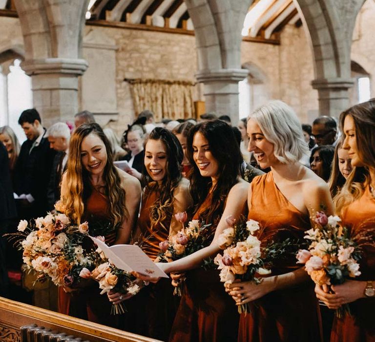 Bridesmaids in one shoulder burnt orange bridesmaid dresses in the alter of Brinsop Court wedding venue 