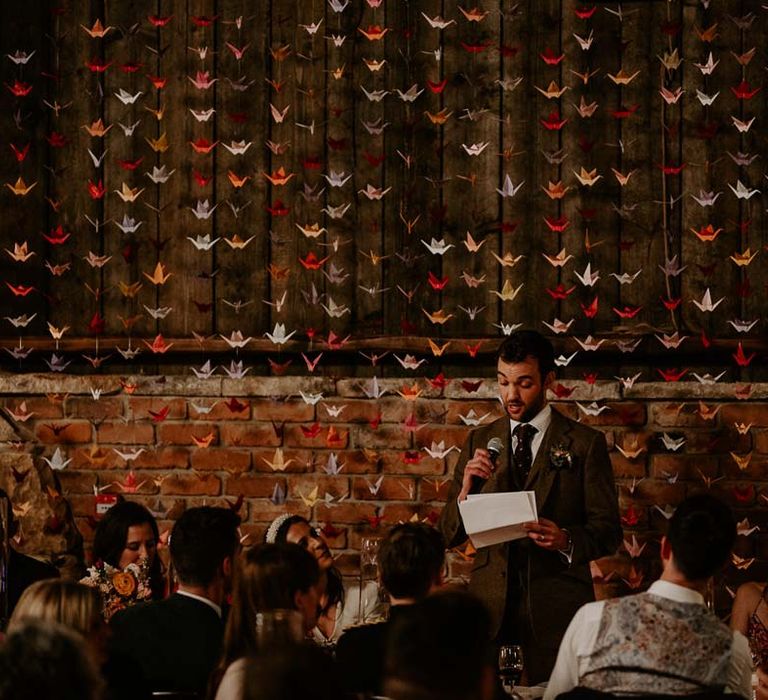 Groom doing grooms speech standing in front of 1000 origami paper cranes DIY wedding decor at Willow Marsh Farm Loughborough 