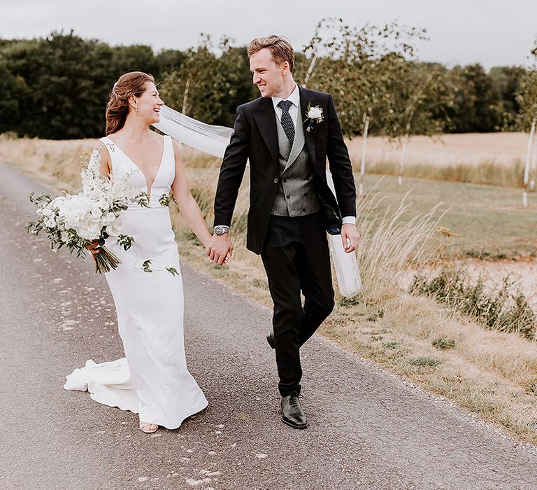 Bride in plunging wedding dress with the groom in three piece suit walking around their venue together 