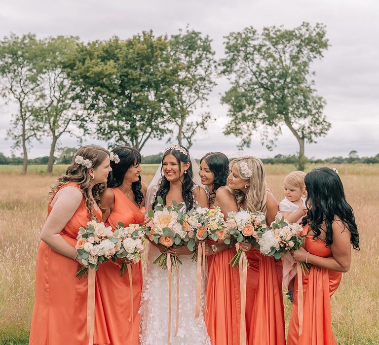 Bridal party wearing matching satin coral bridesmaid dresses with the bride 