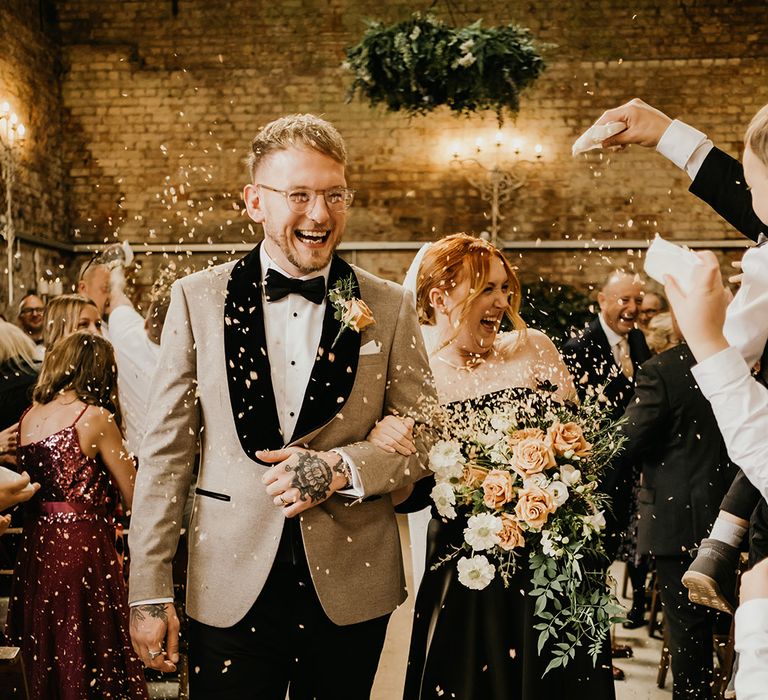 Bride in black wedding dress carrying autumnal wedding bouquet with groom in beige tuxedo 