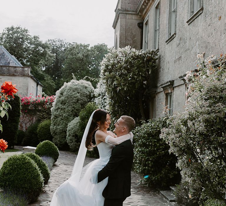 Groom in tuxedo lifting the bride as they share a kiss at country house wedding 