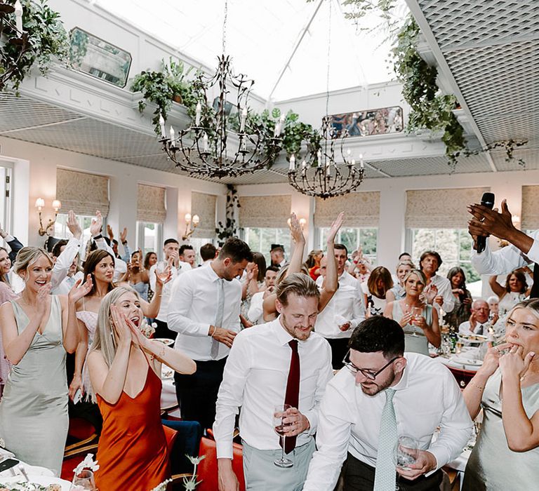 Wedding guests at the wedding breakfast celebrating the wedding by singing and dancing 