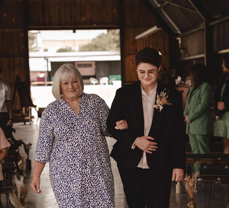 The bride is walked down the aisle by her mother in a spotted blue and white gown 