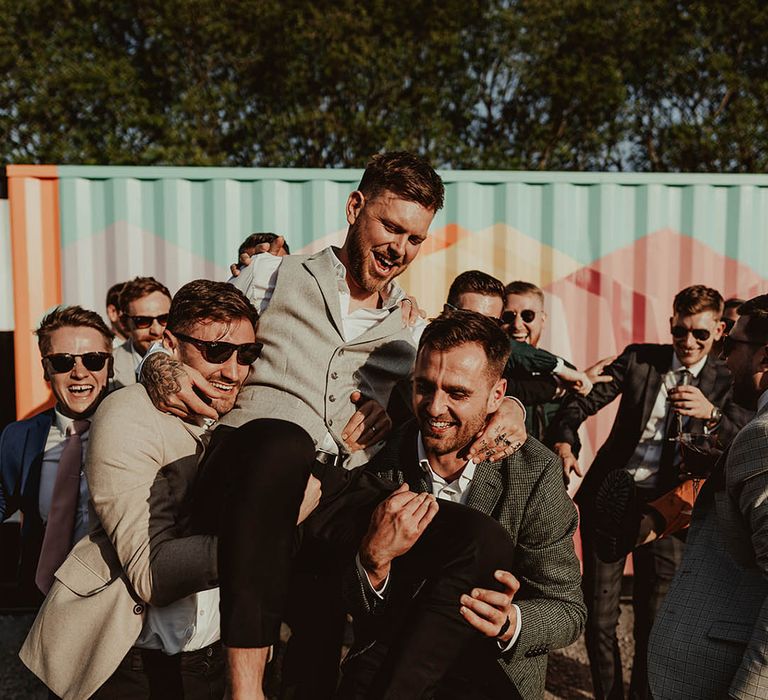 Groomsmen lifting up the groom as they pose for fun group wedding party photos 