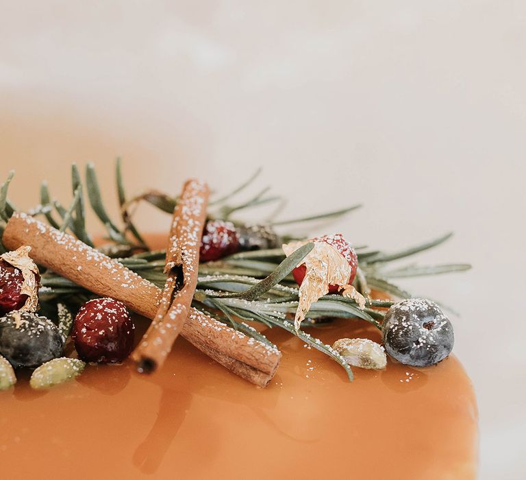 Caramel drip wedding icing topped with cinnamon sticks, berries and evergreen sprigs 