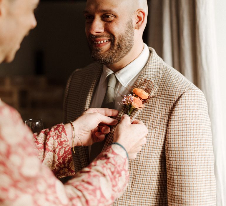 Groom wearing pink flower buttonhole accessory to complement beige suit 