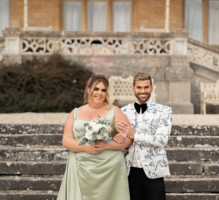 Groom in patterned suit with a bridesmaid in a green bridesmaid dress at country house wedding 