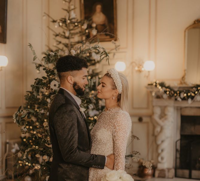 Bride and groom embracing in front of a Christmas tree at festive wedding 