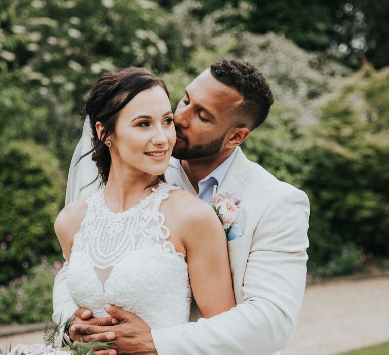 Bride and groom in wedding portrait. He hugs her from behind and they both smile