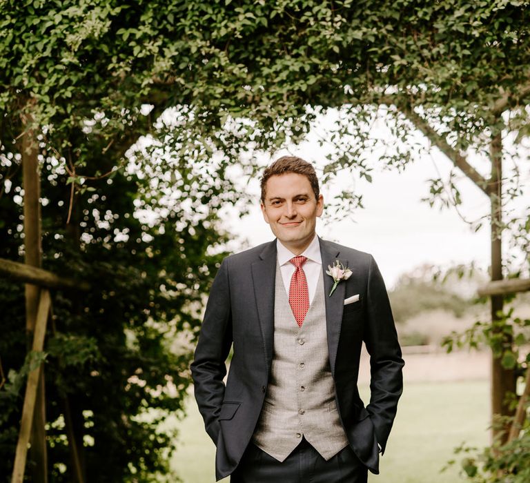 Groom in navy suit with grey waistcoat and red tie 