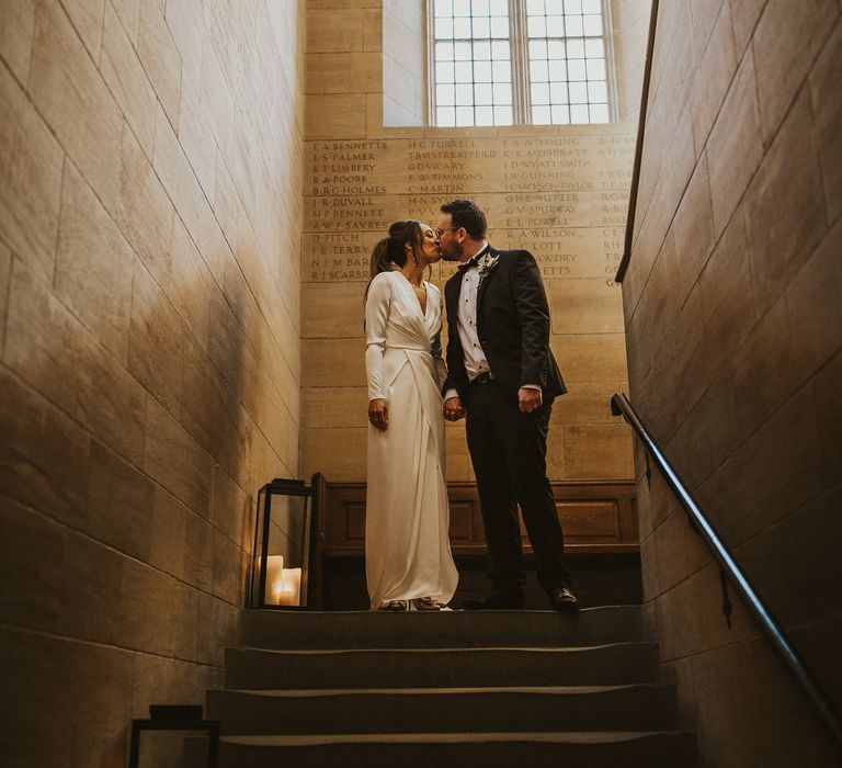 Bride & groom stand together in stairwell with window backdrop 