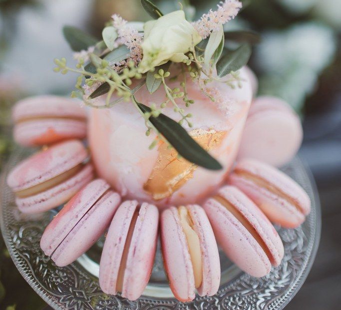 Close up of small pink wedding cake surrounded by pink macarons