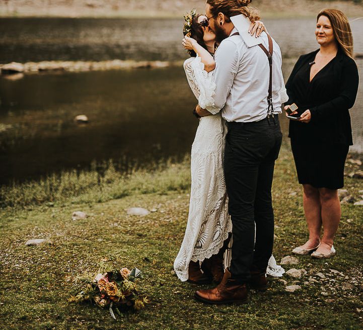 Bride & groom kiss during wedding ceremony with lake in the background