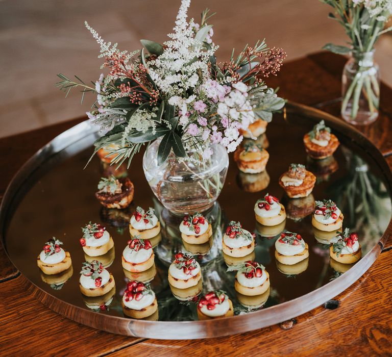 Canapés upon mirrored serving plate with floral bouquet in the middle 