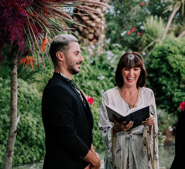 Same sex wedding ceremony with grooms in black suits and celebrant in robe. Photography by Stephanie Shenton.