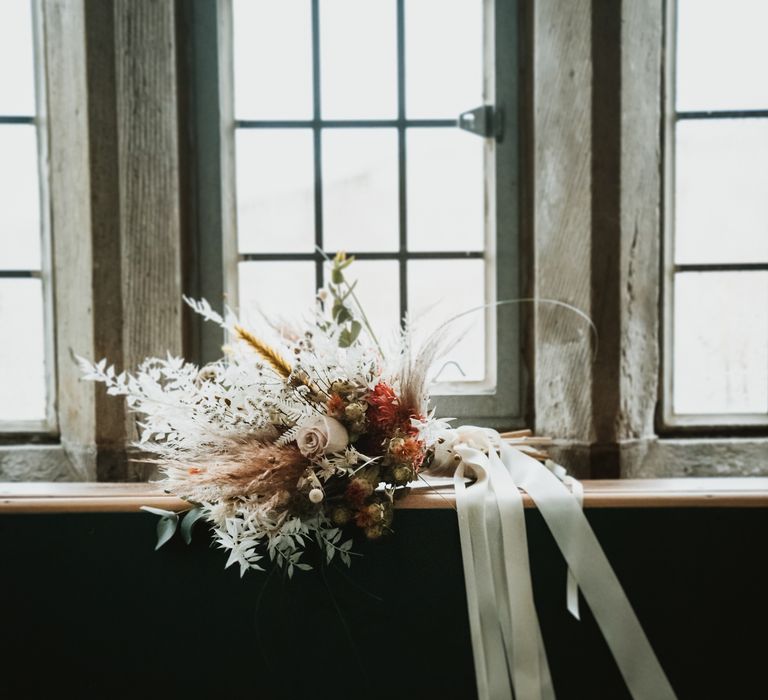 Floral bouquet lays in the window whilst white ribbon drapes down toward the floor