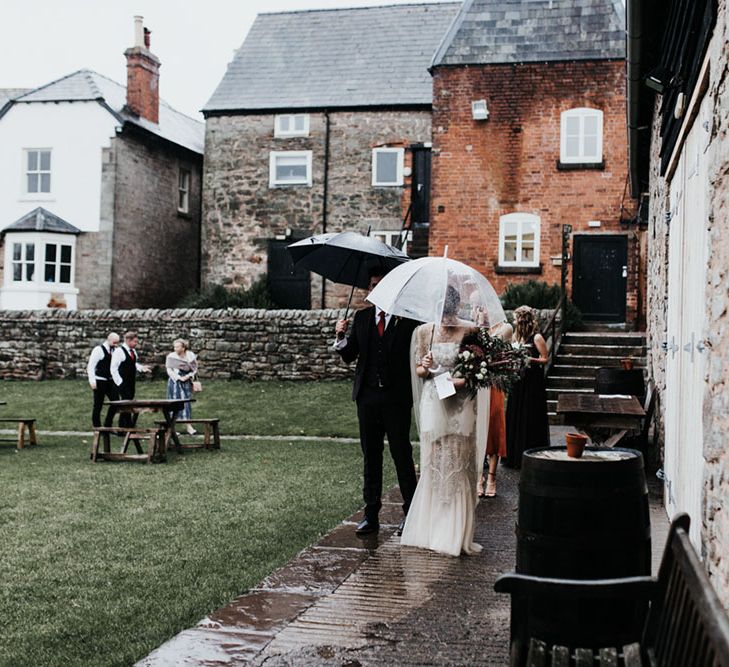 A couple leave their wedding ceremony under a see through umberella in the rain