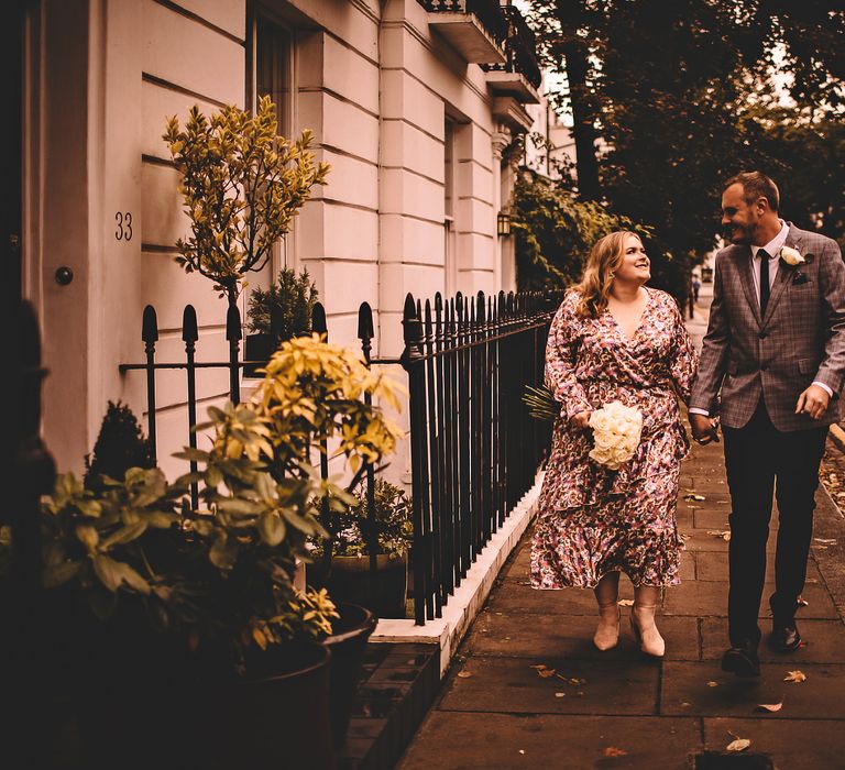 Bride & groom hold hands and walk through Chelsea together as bride carries classic white floral bouquet