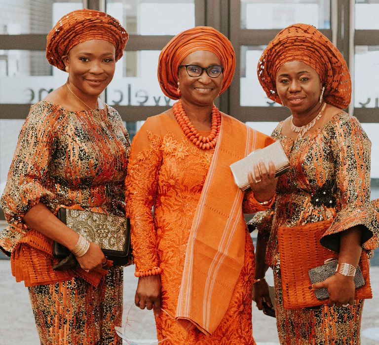 Wedding guest in long orange mermaid style dress and orange headscarf stands in between two wedding guests in long mid-sleeve orange and black printed dresses with orange and black headscarves at Bride Community Church wedding