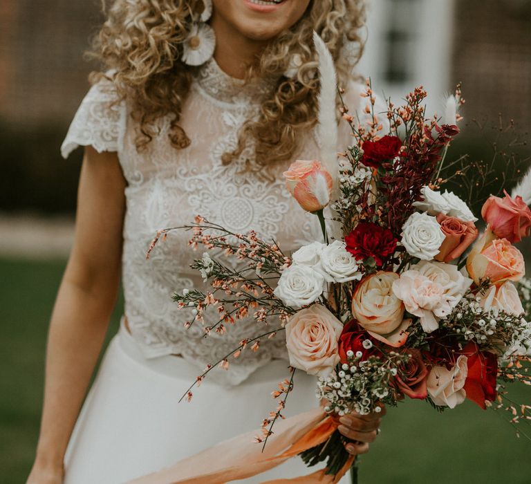 Smiling bride with curly wedding hair holding a bouquet of roses and wild grasses