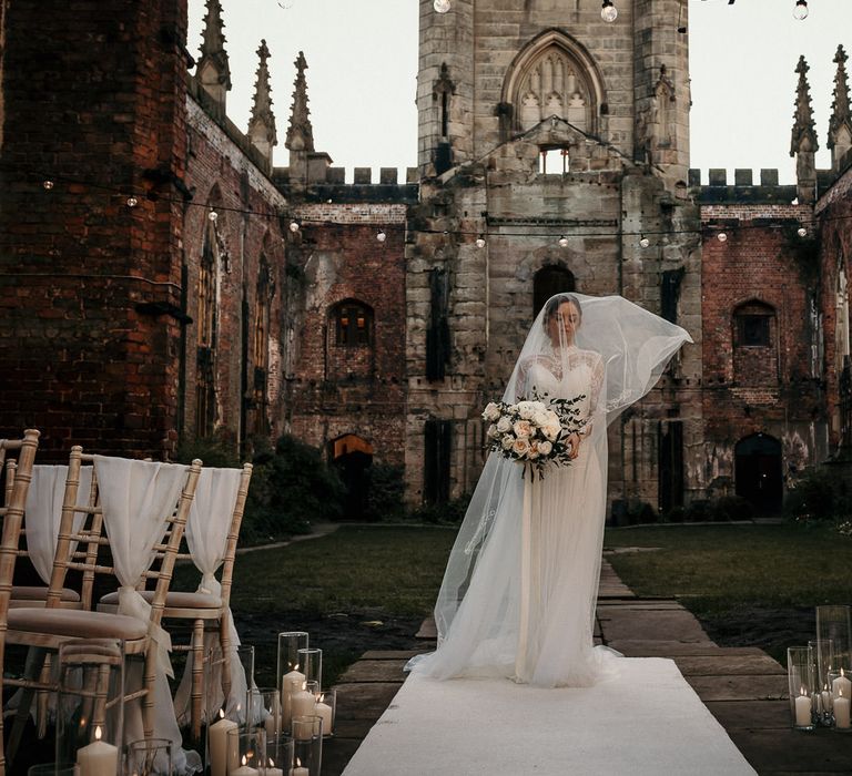 Bride in a lace dress and wedding veil standing at the top of the bomb out church altar 