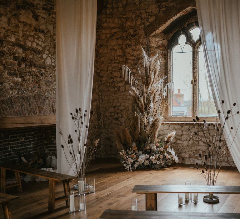 Rustic ceremony room at Pentney Abbey decorated with drapes and dried and fresh floral arrangements 