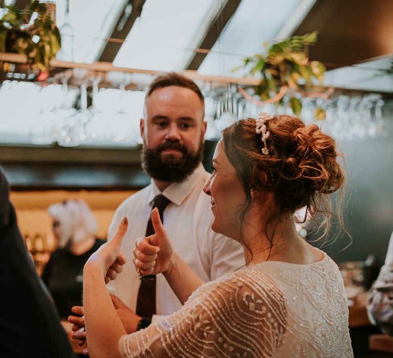 Bride gives thumbs up as she wears her brown hair in curly up-do with bridal crown featuring small pearl flowers