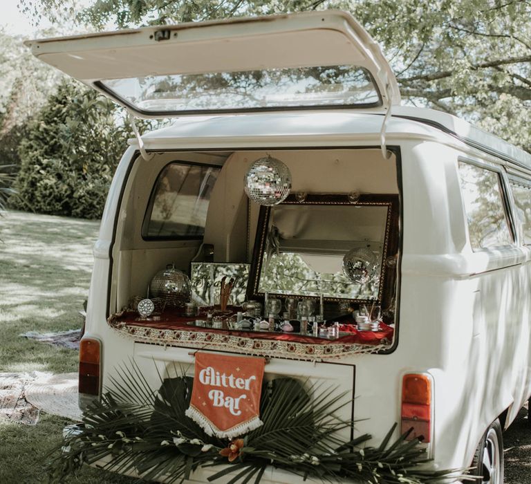 Open back of white campervan with glitter bar set up, disco ball and tropical palm leaf decorations for birds of paradise wedding inspiration