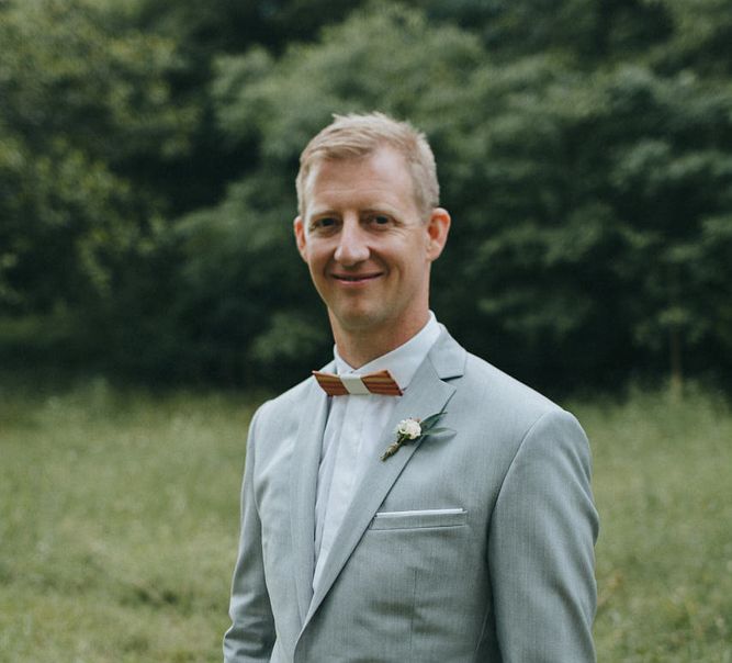 Groom in a pale grey wedding suit with wooden bow tie and white buttonhole flower