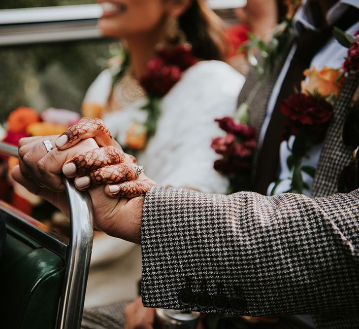 An Indian British bride has her hand on top of her new husbands. You can see her intricate henna on her hand.