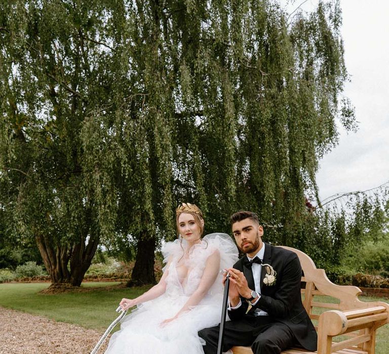 Interabled bride and groom sitting on a bench at Bourton Hall with their walking sticks wearing a tulle wedding dress and black tuxedo 