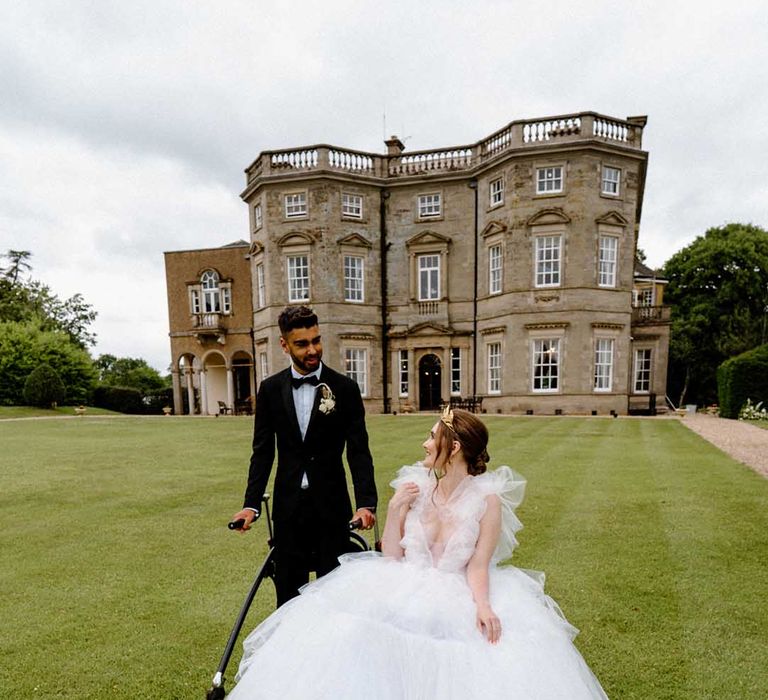 Portrait of a disabled bride and groom in a wheelchair and with a walking frame outside their country house wedding venue 